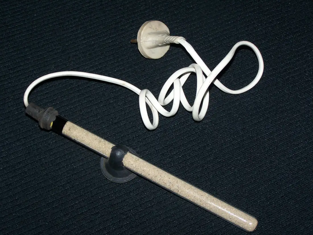 An aquarium heater out of the water: a sand-filled glass tube with a dark cap and indicator at one end, a rubber suction bracket around the middle, and a coiled white cable